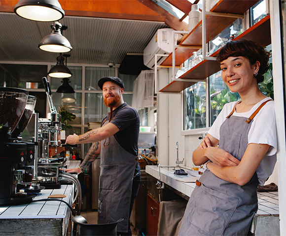 Empresários vestindo avental (um homem e uma mulher), donos de uma cafeteria posam depois de alugar imóvel comercial