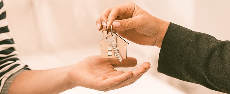 Mão feminina passando chave com chaveiro de casa para outra